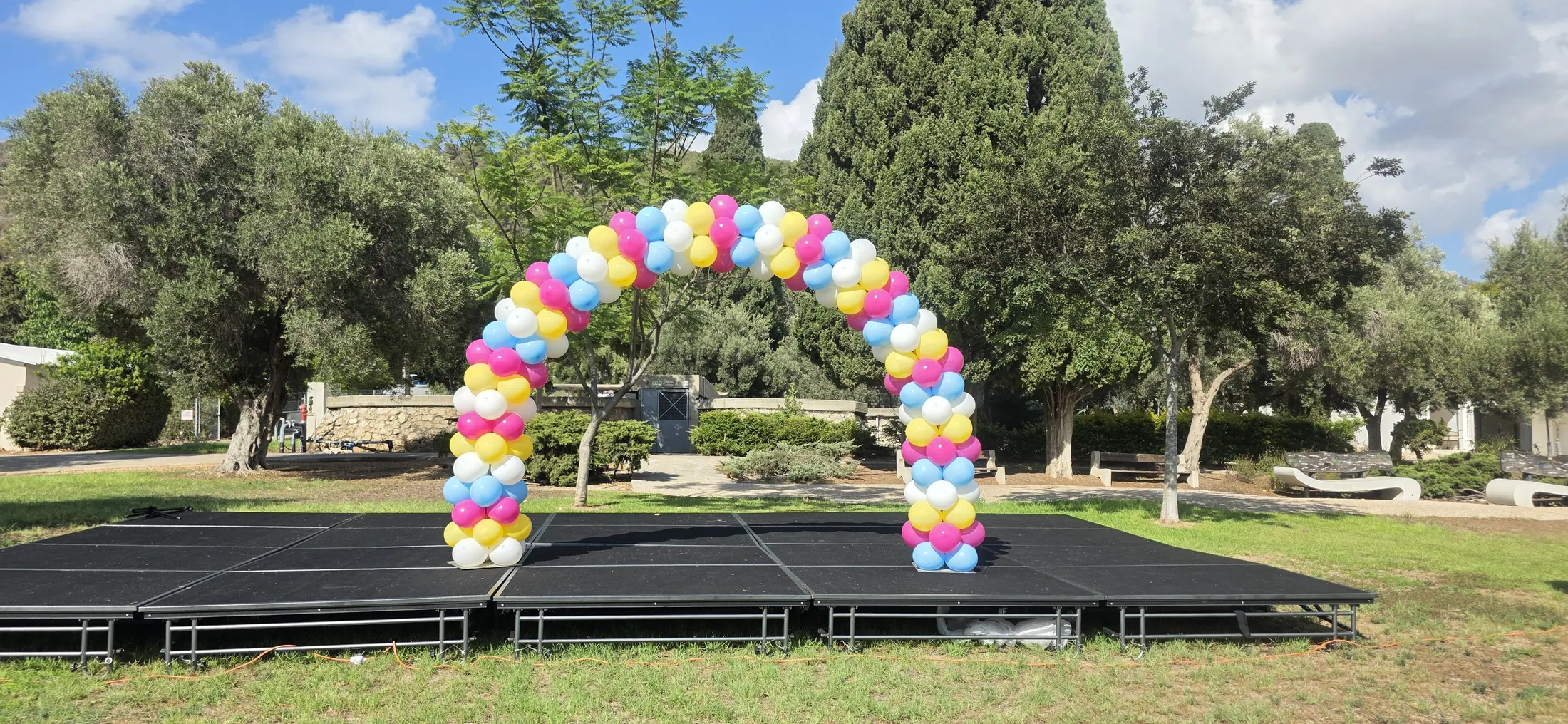 קשת בלונים צבעונית בגוני קשת בחוץ עם עמודים דו-גוניים