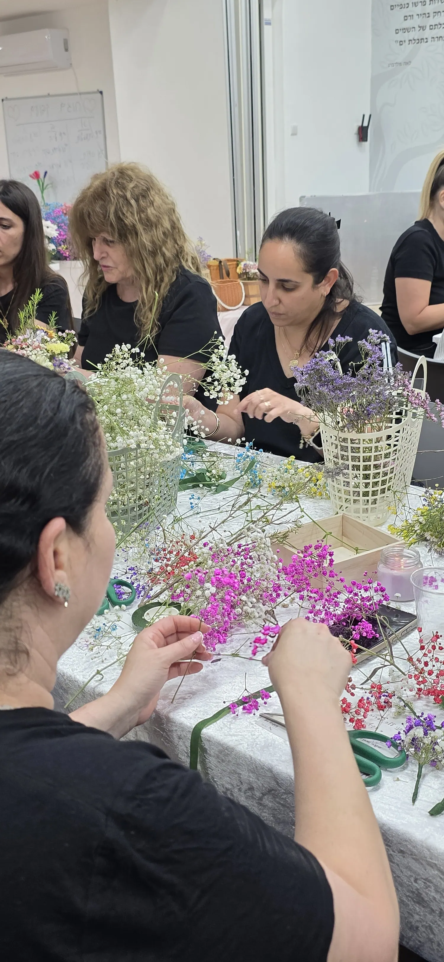 משתתפות בסדנה משזרות פרחים סביב שולחן העבודה