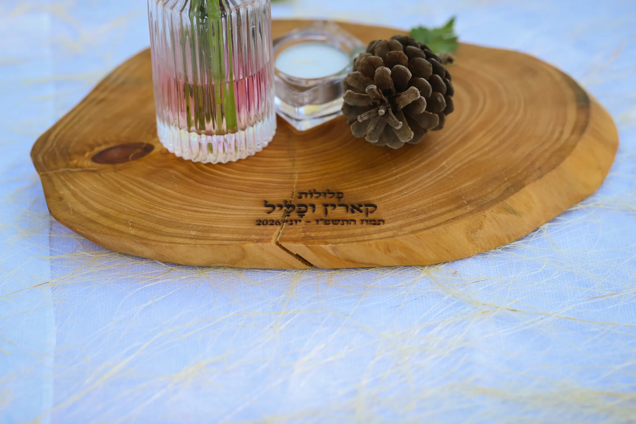 נר בכוס זכוכית לצד אצטרובל על פרוסת עץ מעוצבת